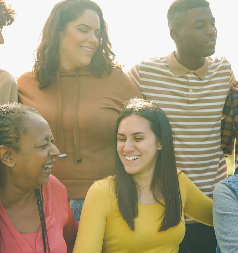 A diverse group of smiling people gathered outside on a sunny day